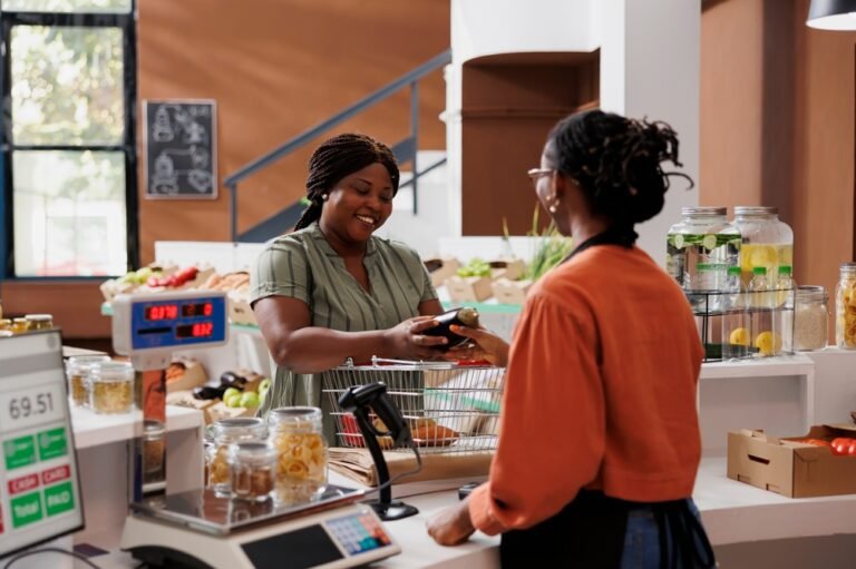 Black,Woman,In,Apron,Assists,Customer,At,Food,Market,Counter.